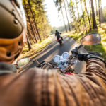 driver's view on motorcycle riding in forest with other motorcyclist