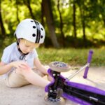 Toddler boy in safety helmet learning to ride scooter