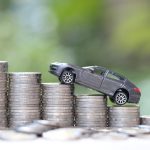 Miniature car model on growing stack of coins money on nature gr