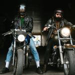 Photo of bearded brutal men bikers on bikes wearing helmets looking at camera in sea port