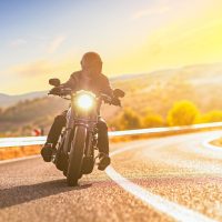 Sunset over an open road and a man with a helmet riding a chopper motorbike